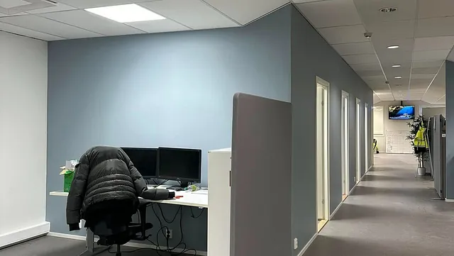 Arbeidsstasjon ved blå vegg i kontorlandskap.