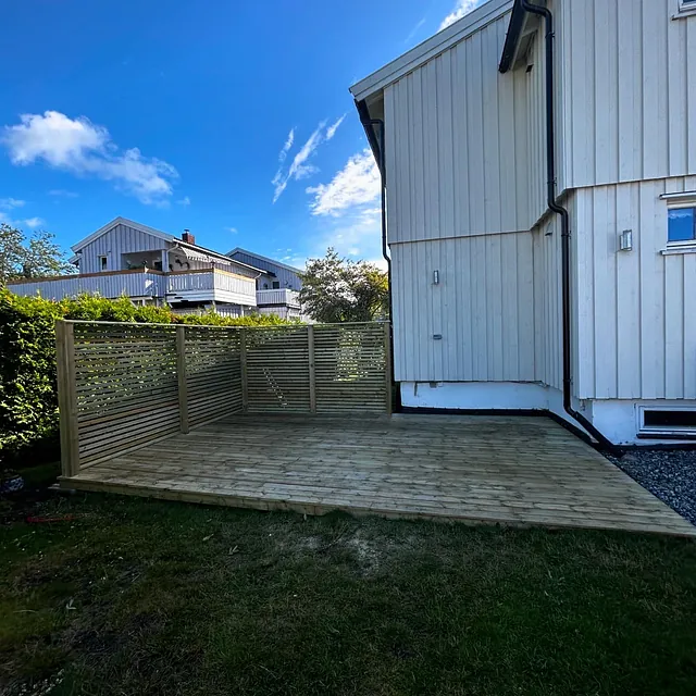 Nybygd treterrasse med levegg ved hvitt hus.