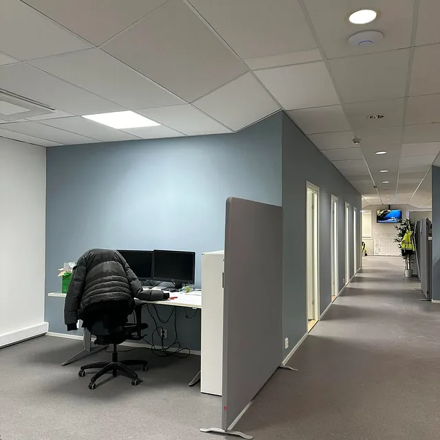 Arbeidsstasjon ved blå vegg i kontorlandskap.