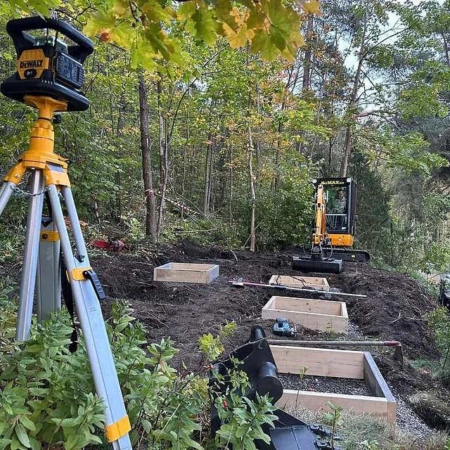 Byggeplass med minigraver og laserutstyr i skog.