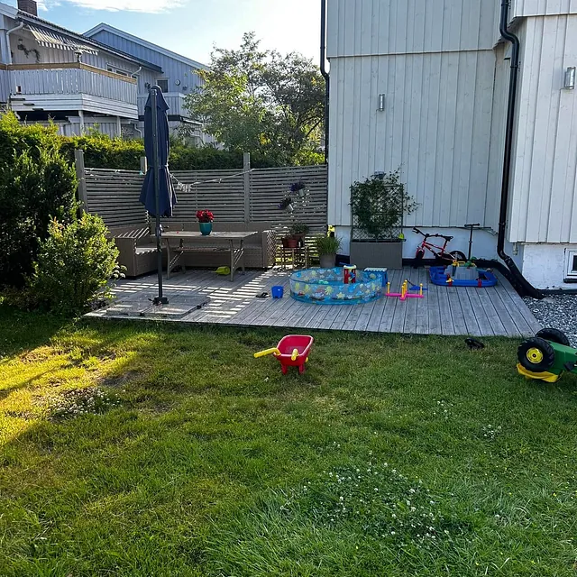Terrasse med møbler, leker og parasoll i hage.
