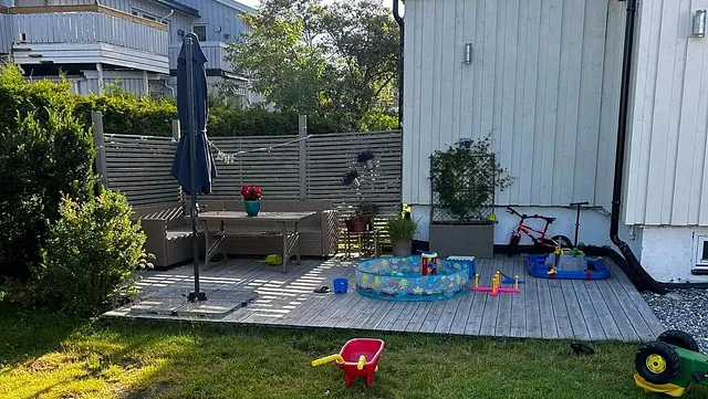 Terrasse med møbler, leker og parasoll i hage.